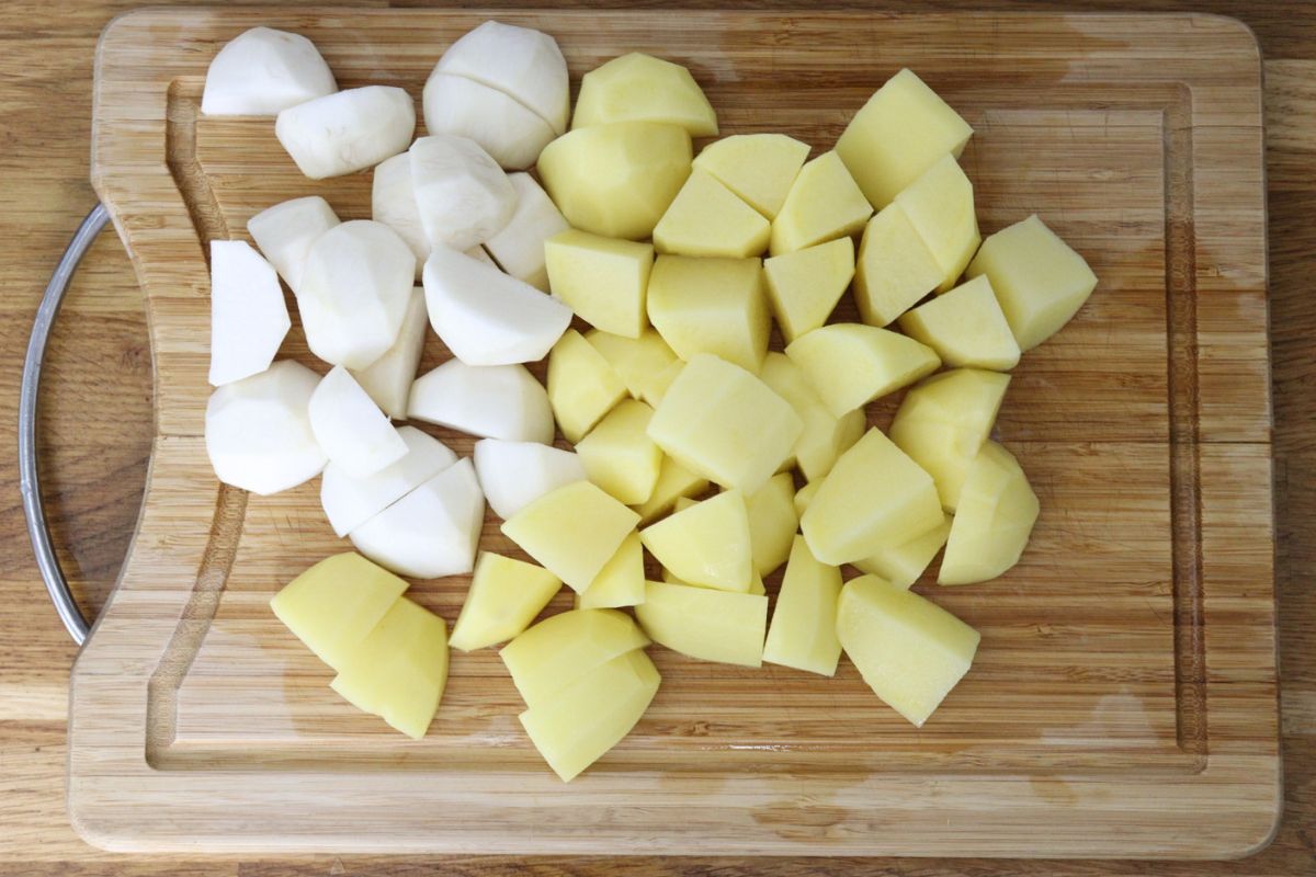 Turnips and potatoes peeled and quartered on a cutting board.