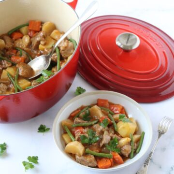 Une assiette de navarin d'agneau à côté d'une cocotte en fonte pleine de navarin.