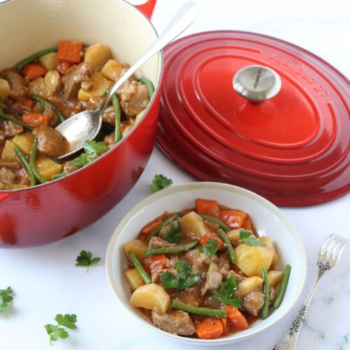 A plate of French Lamb Stew Navarin next to the cast iron Dutch oven where it was cooked.