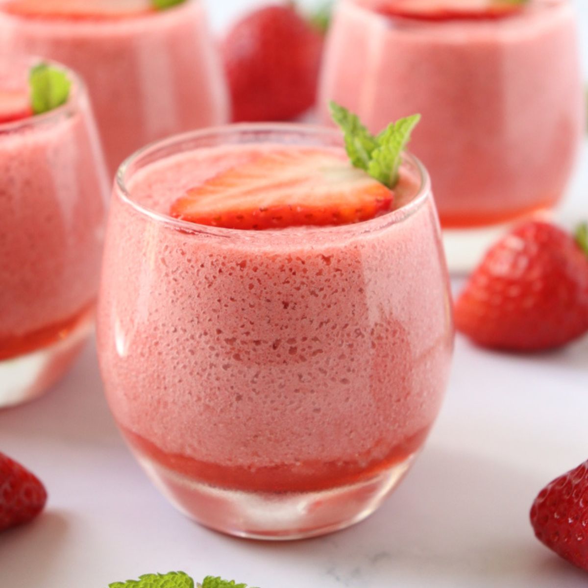 4 verrines remplies de mousse à la fraise, décorée d'une tranche de fraise et de feuilles de menthe.