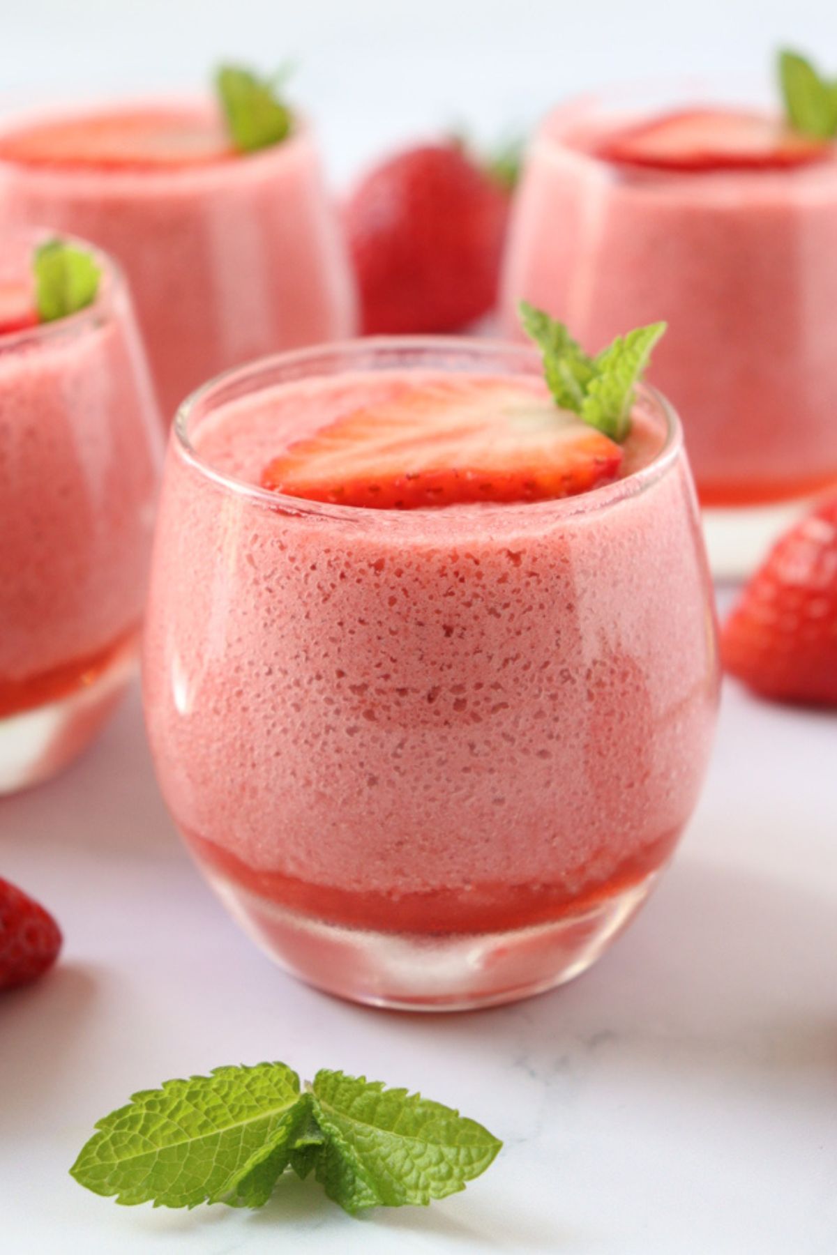 4 glass cups of strawberry mousse decorated with a slice of strawberry and mint leaves.